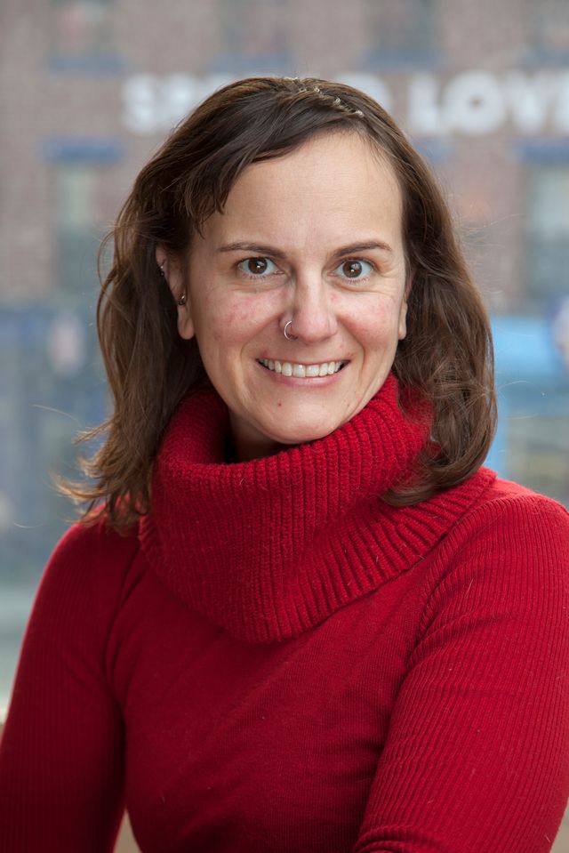 A white woman with long brown hair wearing a red woolly pullover.