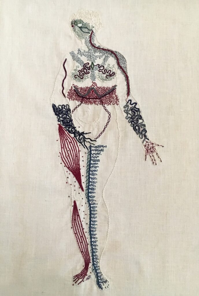 An outline of a naked woman is embroidered on linen in the same bone white colour as the linen. She stands legs together, her right hand covering her groin, her left hand, palm up, extended slightly to her side. Her entire body except for her belly is covered in intricate markings representing different neurological sensations. A longer description is given under the image.