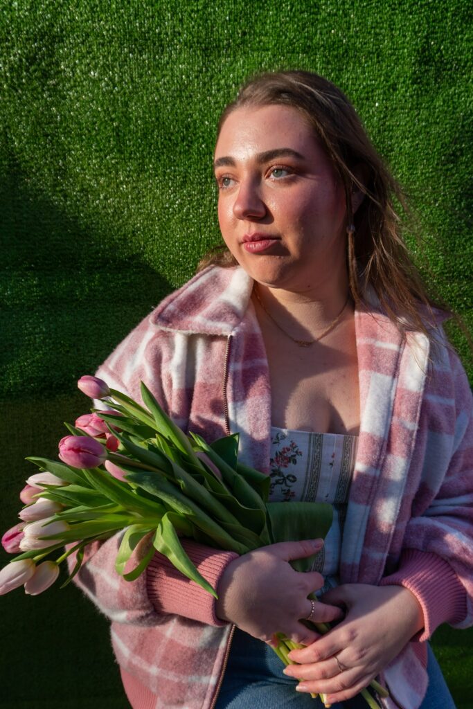 Une femme blanche aux cheveux bruns, vêtue d'une veste polaire rose et blanche, portant un bouquet de tulipes.