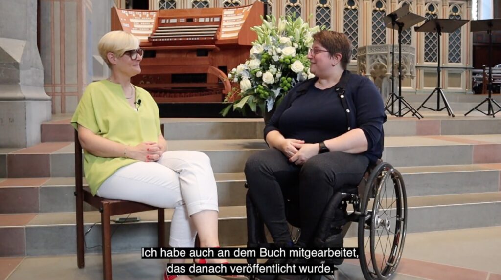 Screenshot of a YouTube interview of Diane by Manuela, with a German subtitle of the captured moment.