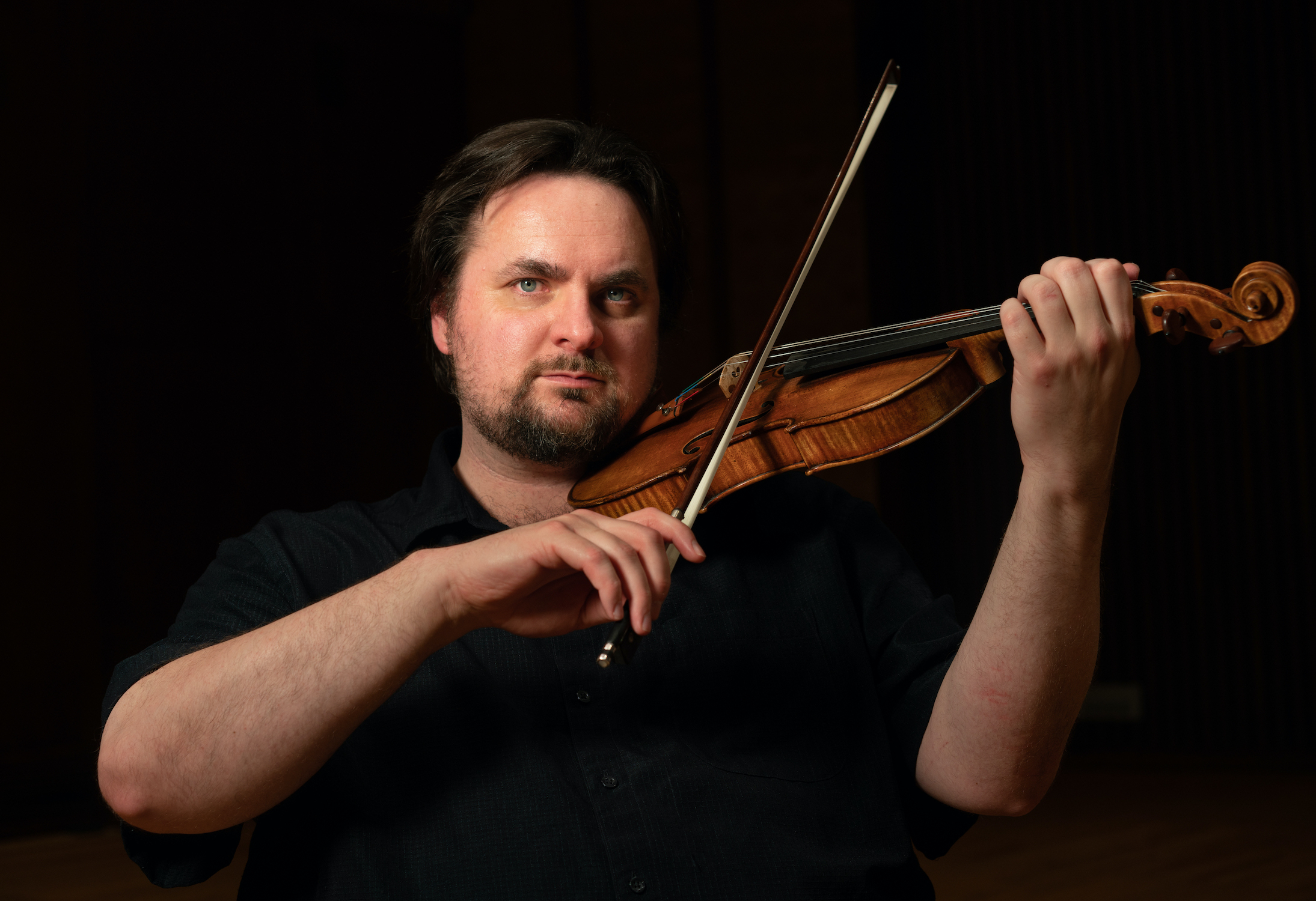 A white man dressed in black, playing his violin.